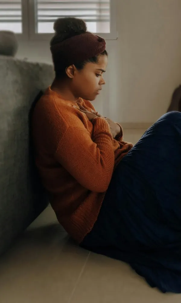Woman sitting with her arms wrapped around herself in striped window light — social anxiety therapy in Los Angeles