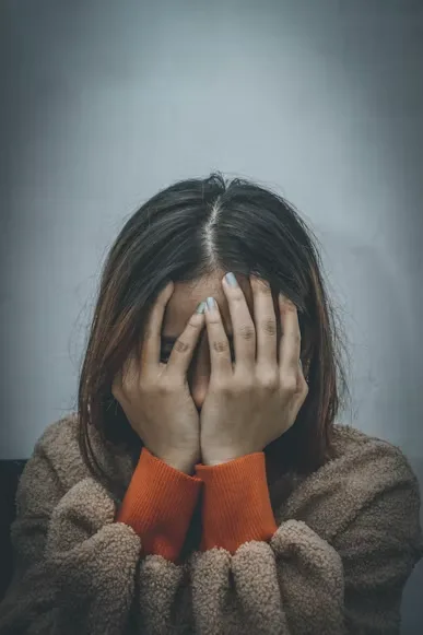 Woman sitting with her face buried in both hands against a grey wall — major depressive disorder and clinical depression therapy in Los Angeles