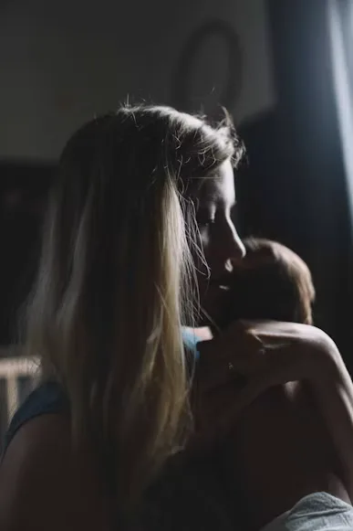 Mother holding her newborn in a dim room, face turned toward the baby — postpartum depression therapy in Los Angeles