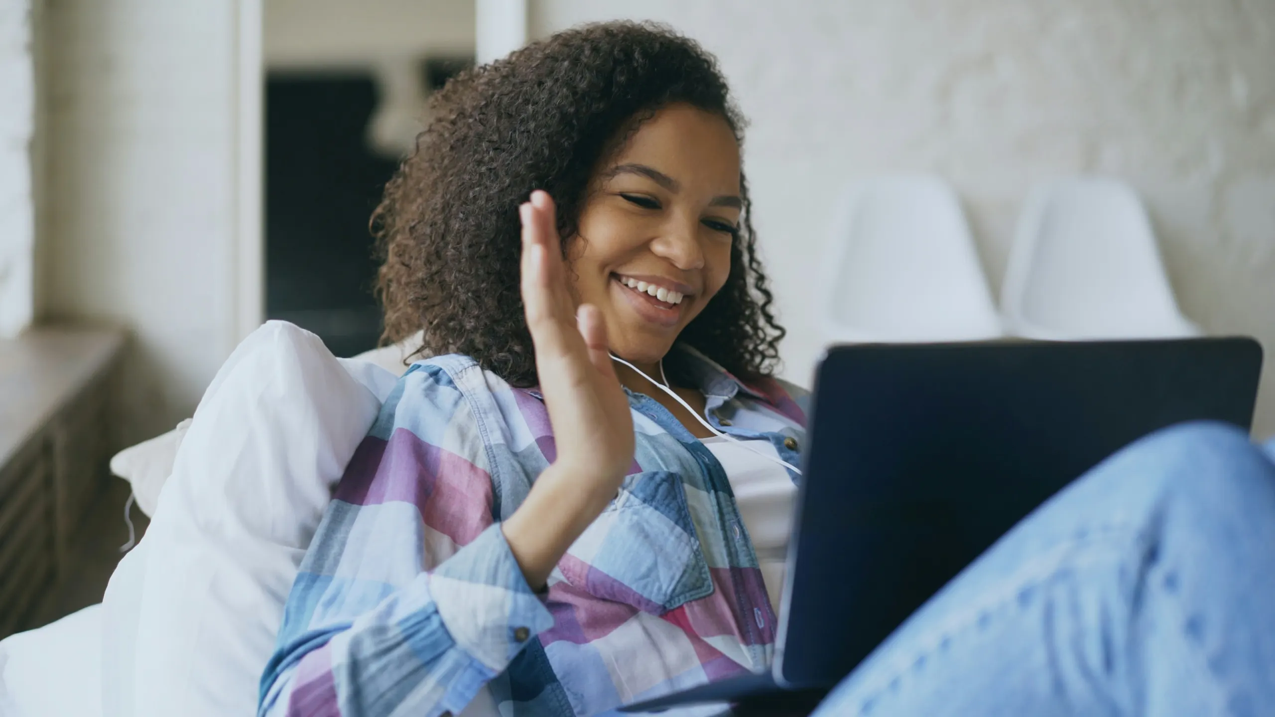 Woman with curly hair waving at her laptop during a video therapy session at home — online therapy in California