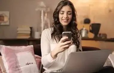 Woman in a warm living room on a video call with her therapist by laptop and phone — online and phone therapy across California