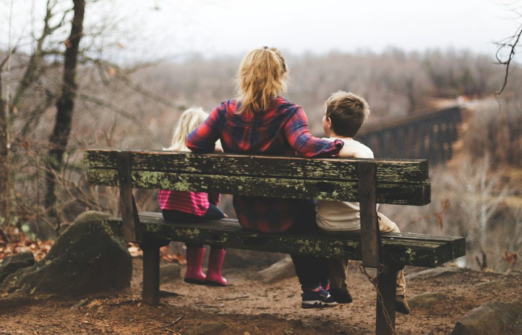 A mother sitting with her two children on a wooden bench, modeling how to express anger with children through healthy emotional regulation.