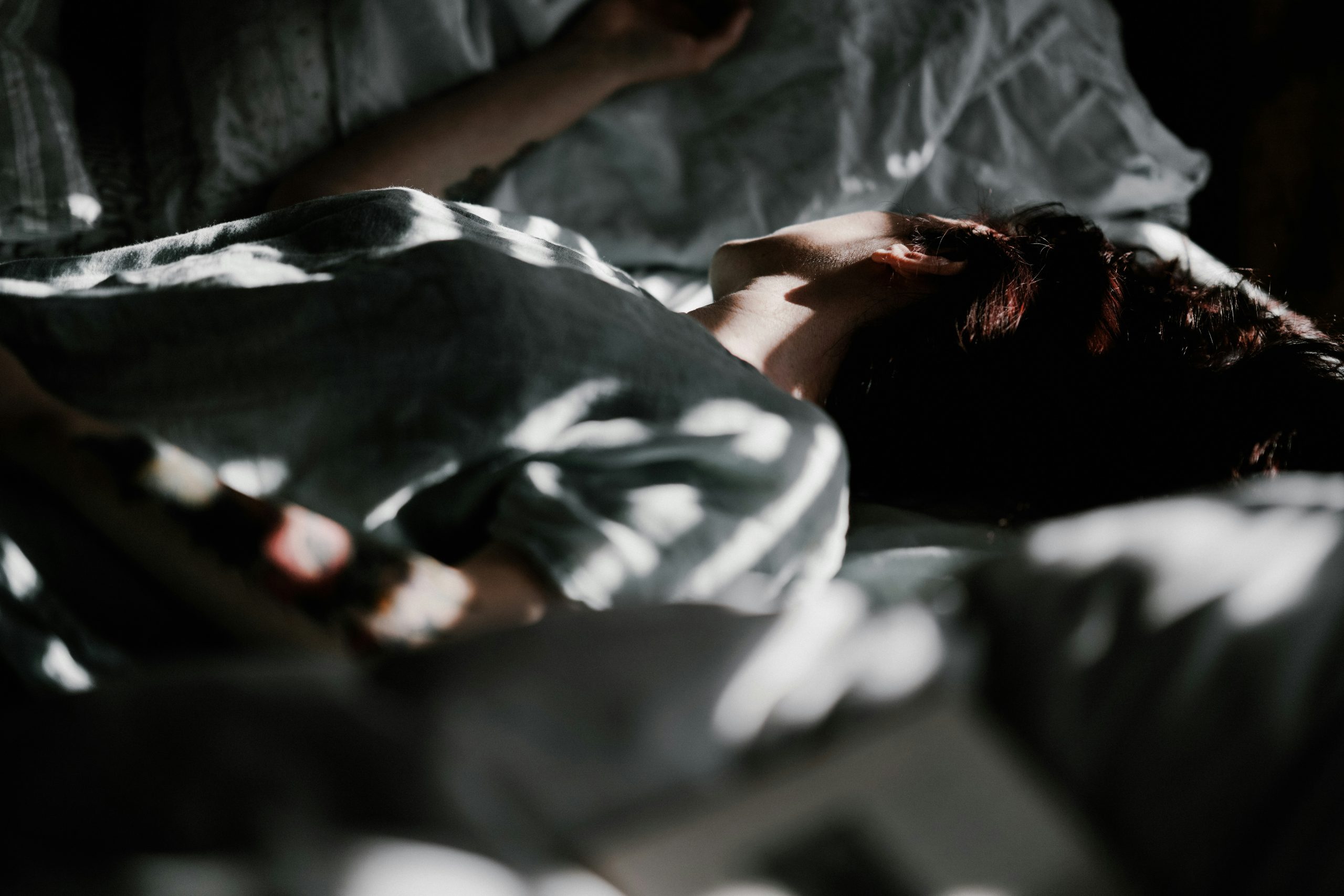 Person lying under a blanket in bed, reflecting the impact of sleep on mental health