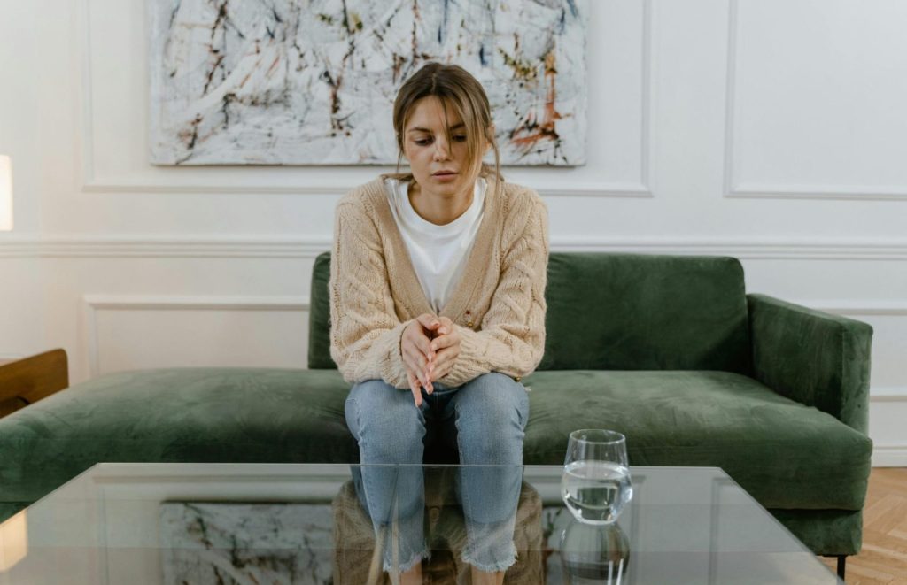 A sad woman sits on a sofa, emotionally withdrawn—representing silent treatment narcissism